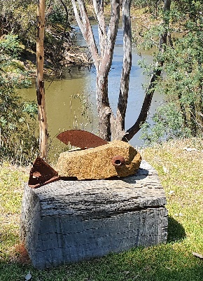 A sculpture of fish made from rock and metal with a river flowing behind it.